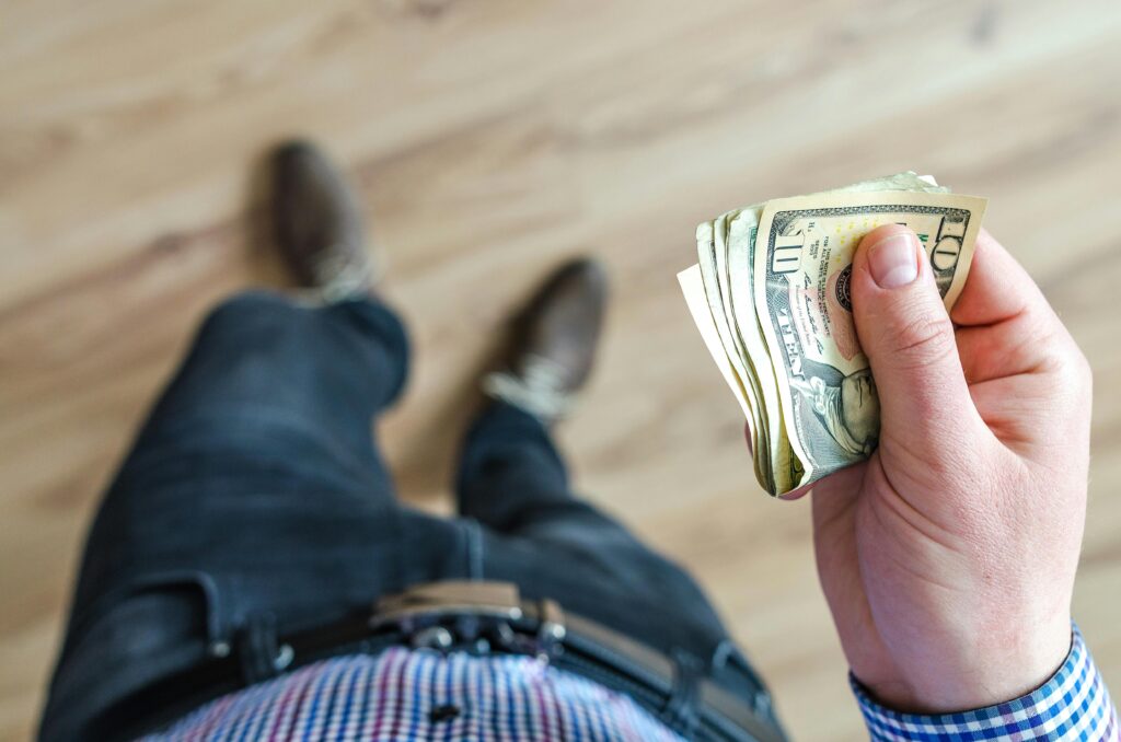 Close-up shot of a man holding US dollar bills indoors with a wooden floor background.